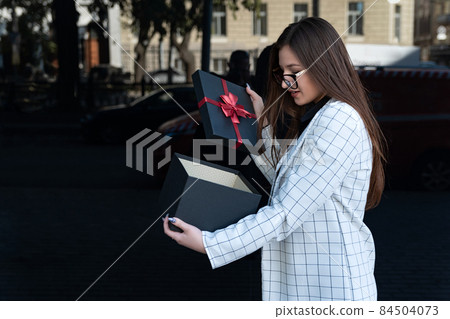 Stylish woman opened gift box. Happy young woman with gift on the street. Girl received a gift and opened it Stylish woman opened gift box. Happy young woman with gift on the street. Girl received a gift and opened it 84504073