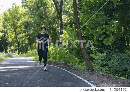 Young woman with weight excess runs in the park. Girl with curvy figure goes in for sports to lose extra pounds. 84504162