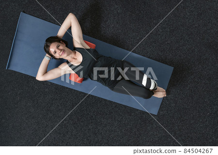 Young pretty smiling sports woman lying on foam roller. Girl doing back massage lying on a mat. Top view Young pretty smiling sports woman lying on foam roller. Girl doing back massage lying on a mat. Top view 84504267