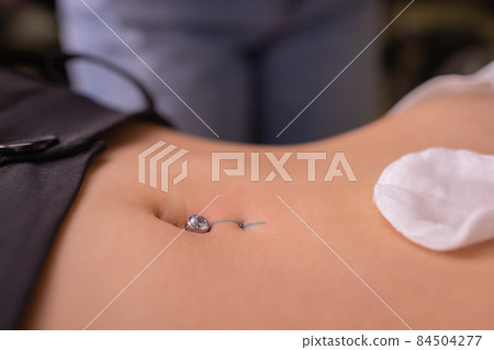The first piercing. Dressing the earrings on the navel. Female piercing. The first piercing. Dressing the earrings on the navel. Female piercing. 84504277