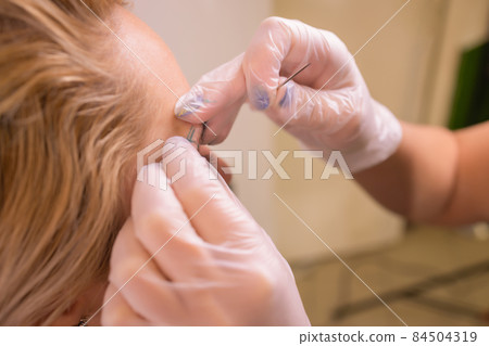Professional placing the jewel of piercing on the temple on the head with ball. Tragus type. Professional placing the jewel of piercing on the temple on the head with ball. Tragus type. 84504319