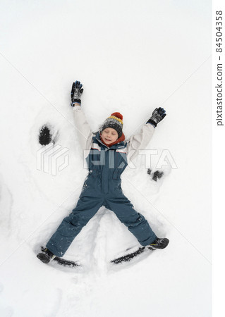 Snow angel made by kid in the snow. Boy lies in the snow. Winter vacation. Top view. Snow angel made by kid in the snow. Boy lies in the snow. Winter vacation. Top view. 84504358