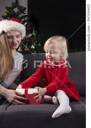 Little girl and mom in Santa hat open Christmas gifts. Little girl and mom in Santa hat open Christmas gifts. 84504405