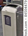 A gray plastic waste basket in a public place 84504479
