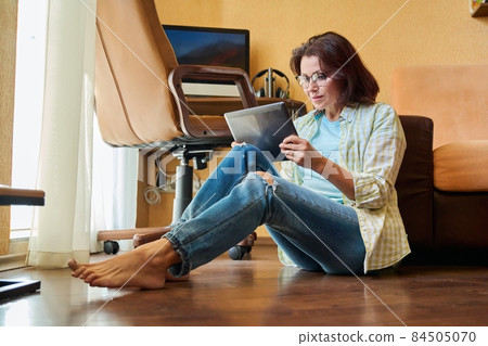 Middle aged woman looking at digital tablet, workplace with computer background Middle aged woman looking at digital tablet, workplace with computer background 84505070