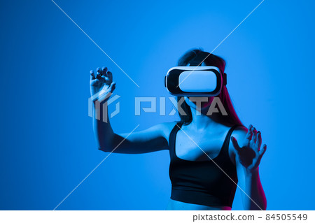 Close up of young woman stands in studio wearing VR glasses and swiping scrolling zooming with hands in a virtual space while interacting with a objects in a metaverse. Virtual reality technology. 84505549