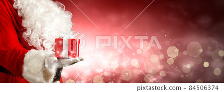 Santa Claus hand holding a wrapped Christmas present. 84506374