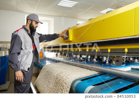 Man operating carpet automatic washing machine in professional laundry service 84510053