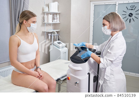 Beautician showing her client special medical equipment. cosmetologist using modern equipment Beautician showing her client special medical equipment. cosmetologist using modern equipment 84510139