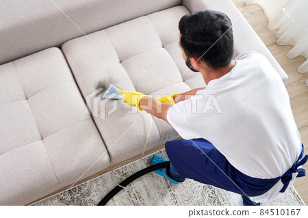 Close-up of housekeeper holding modern washing vacuum cleaner and cleaning dirty sofa with professionally detergent. Professional springclean at home concept Close-up of housekeeper holding modern washing vacuum cleaner and cleaning dirty sofa with professionally detergent. Professional springclean at home concept 84510167