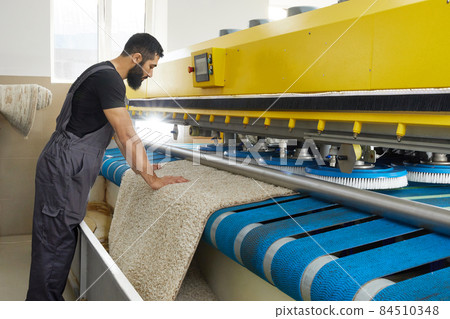 Man operating carpet automatic washing machine in professional laundry service 84510348
