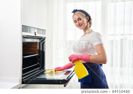 Young woman wearing gloves cleaning oven in the kitchen. Cleaning service concept Young woman wearing gloves cleaning oven in the kitchen. Cleaning service concept 84510480