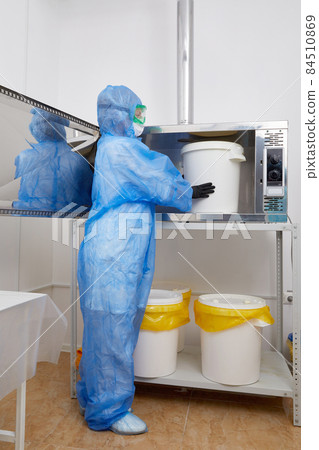 Technologist wearing PPE protective suit, mask, gloves working with big plastic bucket in research laboratory Technologist wearing PPE protective suit, mask, gloves working with big plastic bucket in research laboratory 84510869