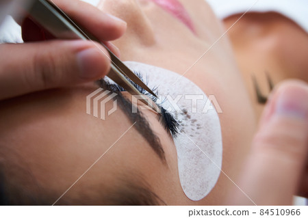 Eyelash extension procedure with tweezers in beauty salon Eyelash extension procedure with tweezers in beauty salon 84510966