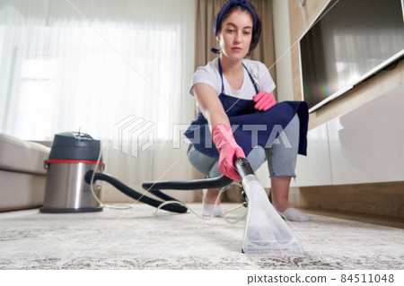 Woman Cleaning Carpet In The Living Room Using Vacuum Cleaner At Home. Cleaning service concept Woman Cleaning Carpet In The Living Room Using Vacuum Cleaner At Home. Cleaning service concept 84511048