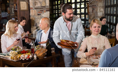 Waiter placing order in front of guests in country restaurant 84511181