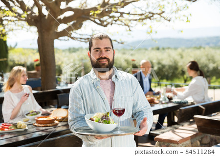 Positive male waiter welcoming guests to country outdoor restaurant Positive male waiter welcoming guests to country outdoor restaurant 84511284