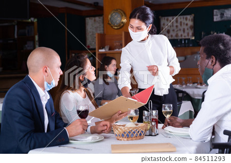 Polite waitress in protective mask consulting restaurant guests 84511293