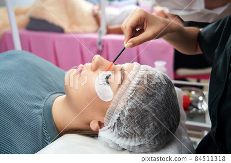 Cosmetologist making eyelash extention and correction using brush 84511318