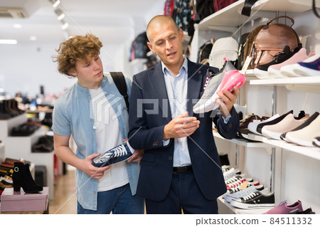 Young father with teenage son looking for sports shoes in store Young father with teenage son looking for sports shoes in store 84511332