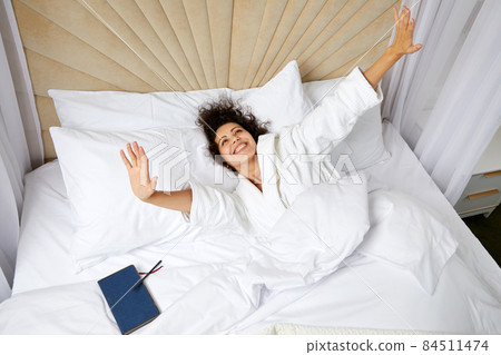 Young smiling Woman Waking Up In Bed And Stretching Her Arms Up, concept of happy beginning of the day 84511474