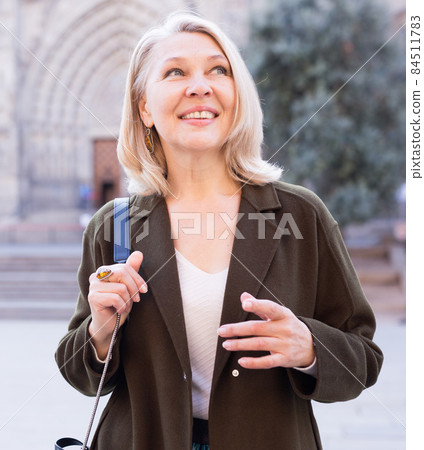 Cheerful mature female is walking in coat on the street Cheerful mature female is walking in coat on the street 84511783