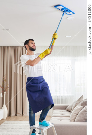 Man cleaning ceiling and lamps in living room. House cleaning service concept. 84511806