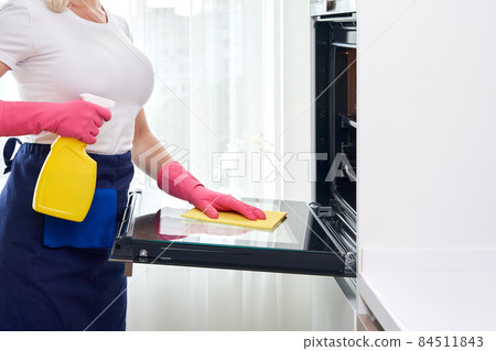 Young woman wearing gloves cleaning oven in the kitchen. Cleaning service concept Young woman wearing gloves cleaning oven in the kitchen. Cleaning service concept 84511843