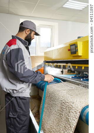 Man operating carpet automatic washing machine in professional laundry service Man operating carpet automatic washing machine in professional laundry service 84511897