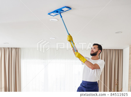 Man cleaning ceiling and lamps in living room. House cleaning service concept. 84511925