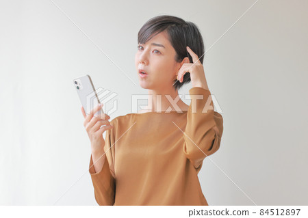 A woman holding a smartphone and putting her finger on her head to think A woman holding a smartphone and putting her finger on her head to think 84512897