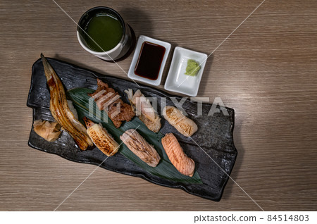 Top view image of grilled Sushi on black plate with green tea cup, grilled variety of healthy Sushi, salmon, tuna, shrimp, beef and Engawa. Top view image of grilled Sushi on black plate with green tea cup, grilled variety of healthy Sushi, salmon, tuna, shrimp, beef and Engawa. 84514803