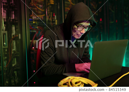 Asian male hacker using a laptop in computer server room 84515349