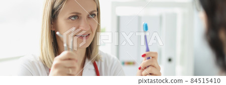 Woman doctor dentist shows patient toothbrush and dental instrument 84515410