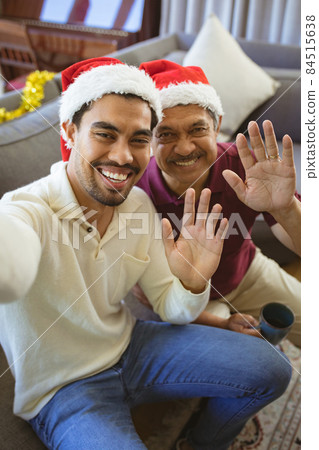 Portrait of happy biracial adult son and senior father in santa hats making christmas video call Portrait of happy biracial adult son and senior father in santa hats making christmas video call 84515638