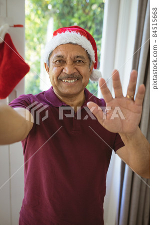 Portrait of happy biracial senior man in santa hat making christmas video call 84515668