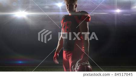 Portrait of confident player wearing jersey holding helmet at illuminated american football stadium 84517045