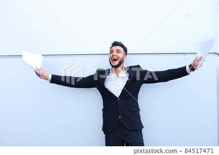 One young adult arab entrepreneur smiling broadly and holds paper on background of wall. One young adult arab entrepreneur smiling broadly and holds paper on background of wall. 84517471