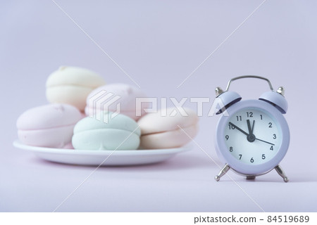 Multi-colored marshmella lies on a saucer. There is a clock nearby. The concept of determining the shelf life of food. Storage period Multi-colored marshmella lies on a saucer. There is a clock nearby. The concept of determining the shelf life of food. Storage period 84519689