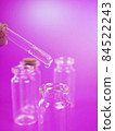 drop of liquid from a pipette into a medical bottle, research concept, new drugs and science, on a bright pink, blue and purple background 84522243