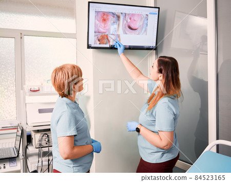Doctor pointing at display while standing beside colleague in gynecological cabinet. Two women gynecologists analyzing results of colposcopy. Concept of gynecology, diagnostics and medical workers. 84523165