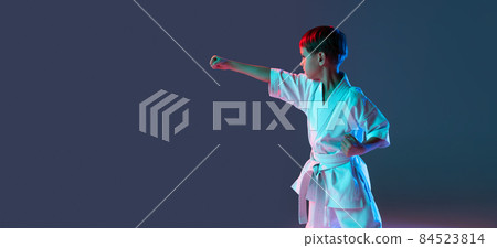 Cropped portrait of boy, karateka training front stance pose isolated over isolated over gradient blue purple background in neon. Flyer Cropped portrait of boy, karateka training front stance pose isolated over isolated over gradient blue purple background in neon. Flyer 84523814