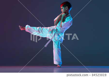 Full-length portrait of sportive child, training karate punching isolated over gradient blue background in neon Full-length portrait of sportive child, training karate punching isolated over gradient blue background in neon 84523819