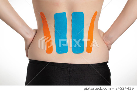 Kinesiological tape orange and blue on the back of the lumbar spine of the girl. Taping problem areas and pain relief 84524439