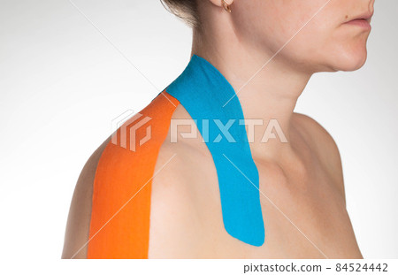 Fixation of muscles and ligaments on the girl's shoulder with blue and orange kinesiological tape, close-up. Taping in sports 84524442