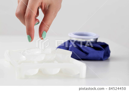 The girl's hand puts a piece of ice into a special medical bag on a white background to relieve swelling and inflammation in case of injury and bruise, close-up 84524450