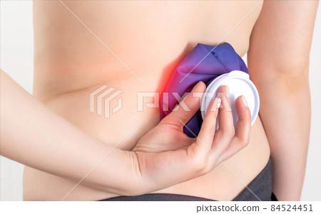 Girl holding a medical ice bag on the back of the spine. The concept of removing puffiness from bruises and injuries of the spine. Removal of pain syndrome, close-up 84524451