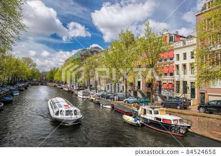 Amsterdam city with tourist boats on canal during springtime in Netherlands. Amsterdam city with tourist boats on canal during springtime in Netherlands. 84524658