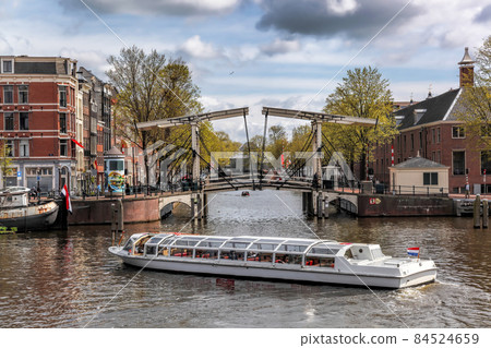 Amsterdam city with tourist boats on canal against old bridge during springtime in Netherlands. Amsterdam city with tourist boats on canal against old bridge during springtime in Netherlands. 84524659