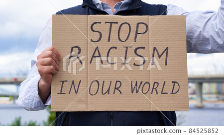 Stop racism concept. Unrecognizable white person holds sign with text against racist. 84525852